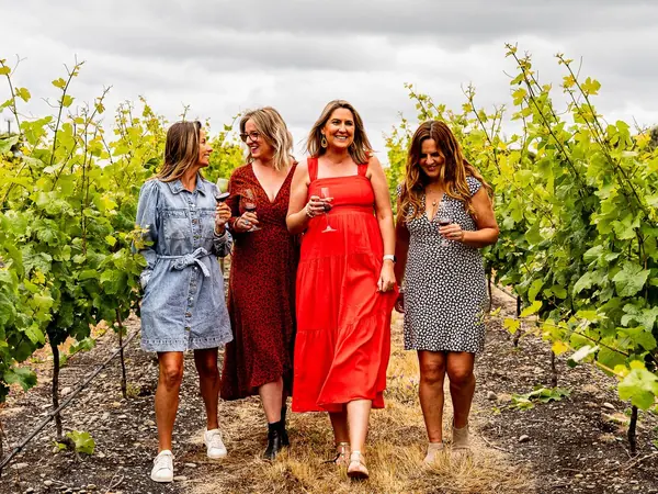 Four guests walking between the vines with glasses of red wine